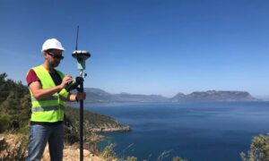 Land surveyor using GPS equipment near a coastal cliff to perform topographic surveys and record tide-based elevation data