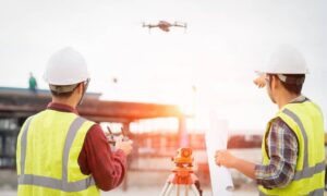 Two surveyors using a drone and tripod equipment during construction staking surveys at an active job site