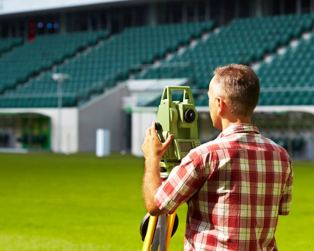 Land surveyor using equipment to perform a boundary and topographic survey on a sports field.