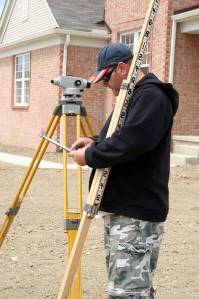 Licensed surveyor taking elevation measurements in front of a house to prepare an elevation certificate for flood zone removal

