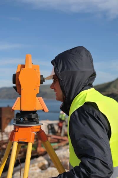Licensed land surveyor conducting a property line survey with equipment near the shoreline
