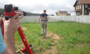 Land survey company measuring a residential property boundary using tripod equipment