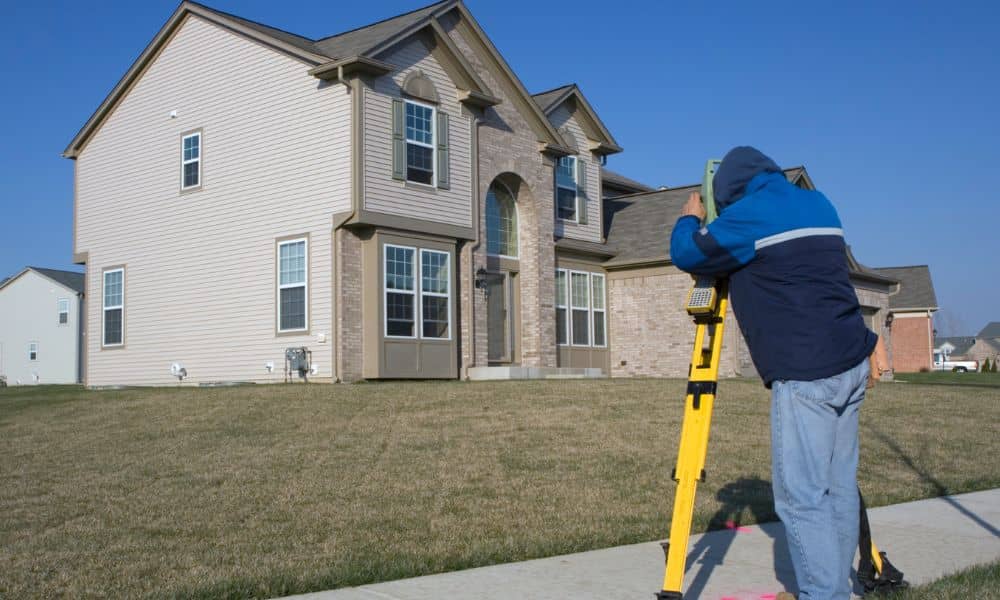 Residential surveyor measuring property boundaries in front of a suburban home