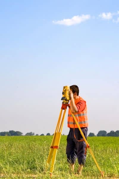 Surveyor measuring property boundaries field - ALTA SURVEY Georgia Surveyor using equipment to measure and confirm property lines during a lot survey before fence installation