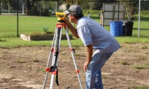 Surveyor measuring a residential property while homeowners look for a property surveyor near me to check boundaries and land conditions