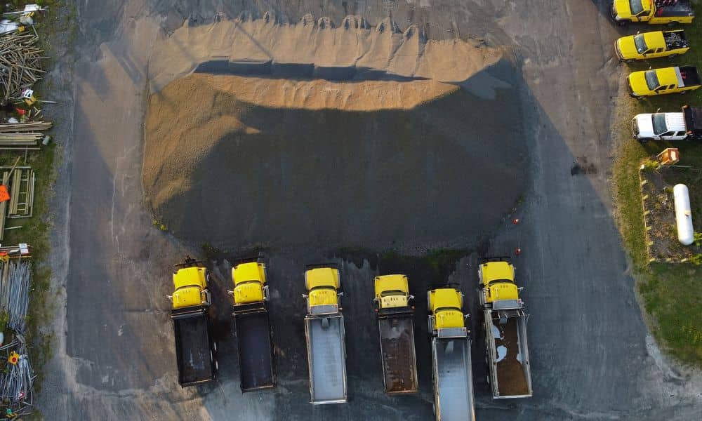 A drone survey captures a large aggregate stockpile surrounded by dump trucks at an active construction site